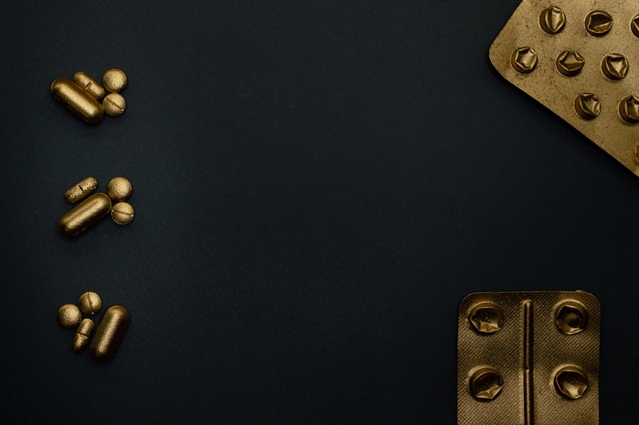 Gold metallic pills and blister packs on a dark surface, highlighting healthcare themes.