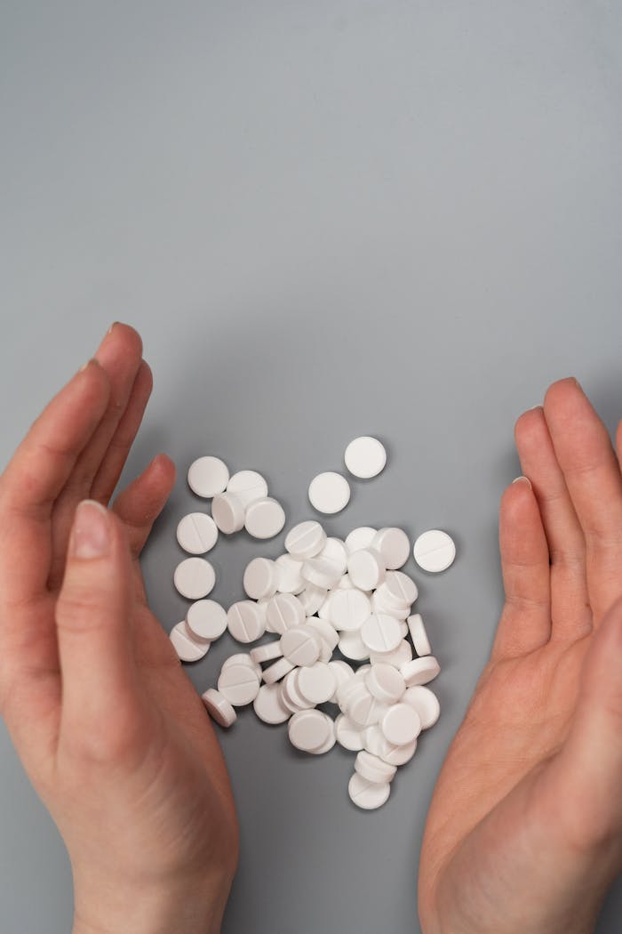 A close-up of hands surrounding white pills on a gray background, symbolizing medication and health concerns.